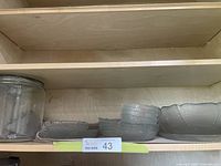 Full set of vintage glass dishes arranged on a shelf showing plates and bowls with detailed rim pattern and the glass cannister jar on the side.