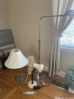 Four lamps placed together on floor near window with curtain, showing varied lamp styles and shapes.