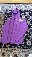 Purple hooded fleece jacket laid flat on a patterned carpet, shows full jacket with zipper and hood.