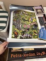 Photo showing the laminated posters stacked, focus on the bird-themed poster titled 'Garden Birds of Greater Vancouver' with detailed illustration of birds and flora.