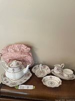 Royal Albert Petit Point China tea set items displayed on a wooden surface with pink floral tea cosy in background.