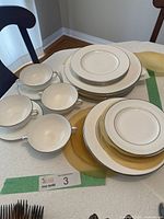 Full view of the china set displaying stacked plates, cups, and saucers on a table with visible silver trim and textured pattern.