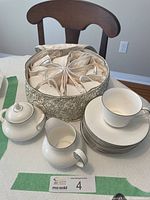 Full view of Royal Doulton Amulet china with teacups nested in fabric divided storage bag, 8 teacups stacked on saucers, creamer pitcher and sugar bowl with lid on white table.