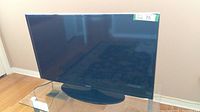 Front view of the Samsung flat screen TV on a glass table, screen off and reflective.
