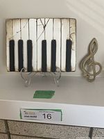 Full view of Sid Dickens piano keyboard art plaque with clear acrylic stand and brass music note.