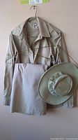 Beige XL Tilley button-up long sleeve shirt with hanger, beige shorts and Tilley wide-brim life guarantee hat hanging on a wall