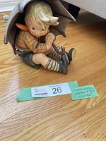Front view of seated boy under umbrella on hardwood floor alongside auction lot card