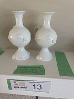 Front view of two white clay cruets with sculpted face designs