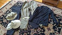 Overview of two pairs of MEC pants, two full-brimmed hats, and a wool long sleeve top arranged on a rug