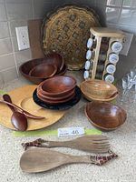 View of wooden salad bowls, black painted bowl, turned wooden bowls and plate, spice rack with jars, and giraffe salad tongs on countertop