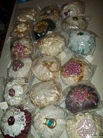 Lot of 18 handmade fragrant sachets displayed in plastic bags, showing various fabric types, colors, and ornamental designs