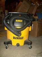 Front view of the DeWalt 5 gallon wet/dry vacuum cleaner showing the yellow and black body with black hose coiled around the top and four caster wheels at the bottom.
