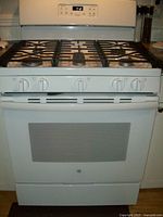 Front view of the white GE gas stove showing five burners, control knobs, and oven door with window.