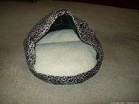 Front view of a hooded pet bed with fleece lining and leopard print fabric, showing the entrance and interior cushion.