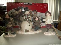 Front view of the four-piece children and snowman scene set with original packaging visible in background.