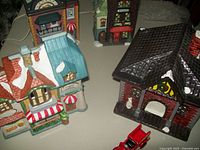 Overview of three ceramic Christmas village houses showing snow-covered roofs, including a tavern and fire station.