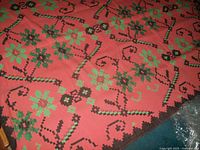 Close-up of the rug pattern showing green and dark brown pixelated floral designs on pink background and zigzag border.