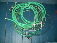 Photo showing three short green garden hose pieces with metal connectors, attached to two sprinklers and one nozzle.