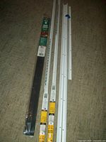 Full view of the storm door closure set alongside three white strips of doorway weather stripping all laid on carpet.