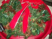 Close-up view of the decorative Christmas wreath with pine cones, red berries, and a large red bow on top.