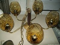 Shows side angle view of chandelier with wooden stem, brass-colored arms and 5 amber swirl glass globes.