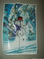Printed photo showing the snowman lawn ornament illustrated in a winter landscape background with snow-covered trees, depicting how it would look outdoors.