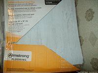 Photo showing packaging label of Armstrong vinyl floor tiles with tile partially pulled back to show color and texture.