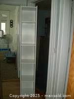 Front view of white melamine tower bookcase showing its tall, narrow structure and four shelves.