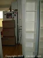 Tall white melamine tower bookcase shown standing next to cardboard boxes and other background items, showcasing the full height and shelf spacing.