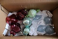 10 assorted large glass Christmas ornaments in a box, showing different shapes and colors including red, green, turquoise, and silver pieces.