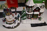 Two Christmas village pieces displayed on a flat surface, showing the Nutcracker scene and house with snow-covered roofs and holiday decorations.
