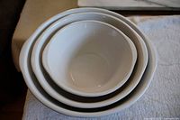 Three nested white ceramic mixing bowls, showing interior and exterior view with decorative pattern and size differences