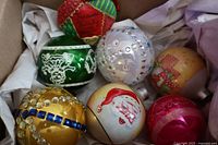 Top view of the 7 vintage glass Christmas tree ornaments in a box with tissue paper, showing varied colors and decorative details