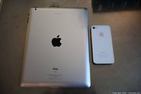 Photo of the back of Apple iPad and back of Apple iPhone 6 placed on a surface showing device condition and logos.