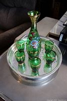 Green glass cordial set showing one decanter and six cups on a round silver-plated tray with beaded edges.
