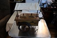 Full view of old hand made wooden fish cart with fabric canopy, wooden wheels, and painted fish on the side.