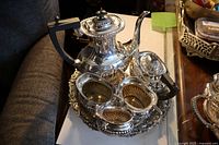 Full view of the six-piece silver plated tea set on an ornate round tray showing teapot, sugar bowl, creamer, waste bowl