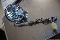 Full view of the searchlight showing the round reflector, metal extendable arm, wiring, and cream-colored handle