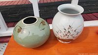 Both pottery pieces: round green vase with butterflies and taller white vase with floral and butterfly designs.