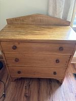 Frontal view of the antique wooden dresser showing the three drawers and the triangular backboard with round wooden pulls.
