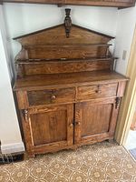 Front view of sideboard showing overall structure: upper shelf with central finial, two drawers, and two-door cabinet base