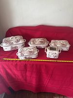 Full view of five-piece Florentine ceramic casserole and serving set arranged on red fabric background, showing all dishes with lids and sauce dish with handles.