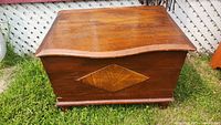 Full view of the antique wooden blanket box with curved top placed outdoors on grass with decorative front panel.
