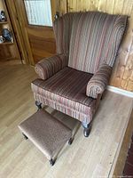Full view of the antique parlour wingback chair with matching footrest, showing upholstery and wooden legs.