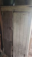 Front view of pine cupboard showing vertical plank doors, metal hinges, wooden handle, and wear on wood surface.