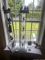 Full view of two tall cardinal-themed candle holders placed side by side on a window ledge. Both silver metal with frosted glass decorated with red cardinal bird images. One holder topped with three cardinal bird figurines and 'WELCOME' sign.