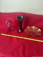 Photo showing all three items: cranberry Carnival Glass vase, bowl and clear pinkish glass pitcher on red background with measuring tape