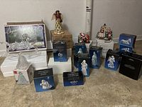 Full lot overview showing multiple boxed and unboxed Christmas figurines including glass rocking horse, angels, nativity figures, Santa Claus and Victorian couple.
