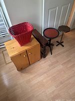 Photo showing the wooden bedside table, red wicker basket on top, narrow dark wood table, small round table with red top, and hexagonal wooden table.
