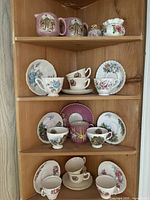 Wooden corner shelf displaying a collection of vintage cups and saucers including chintz and Baileys patterns in pink, blue, floral and other designs across three shelves.